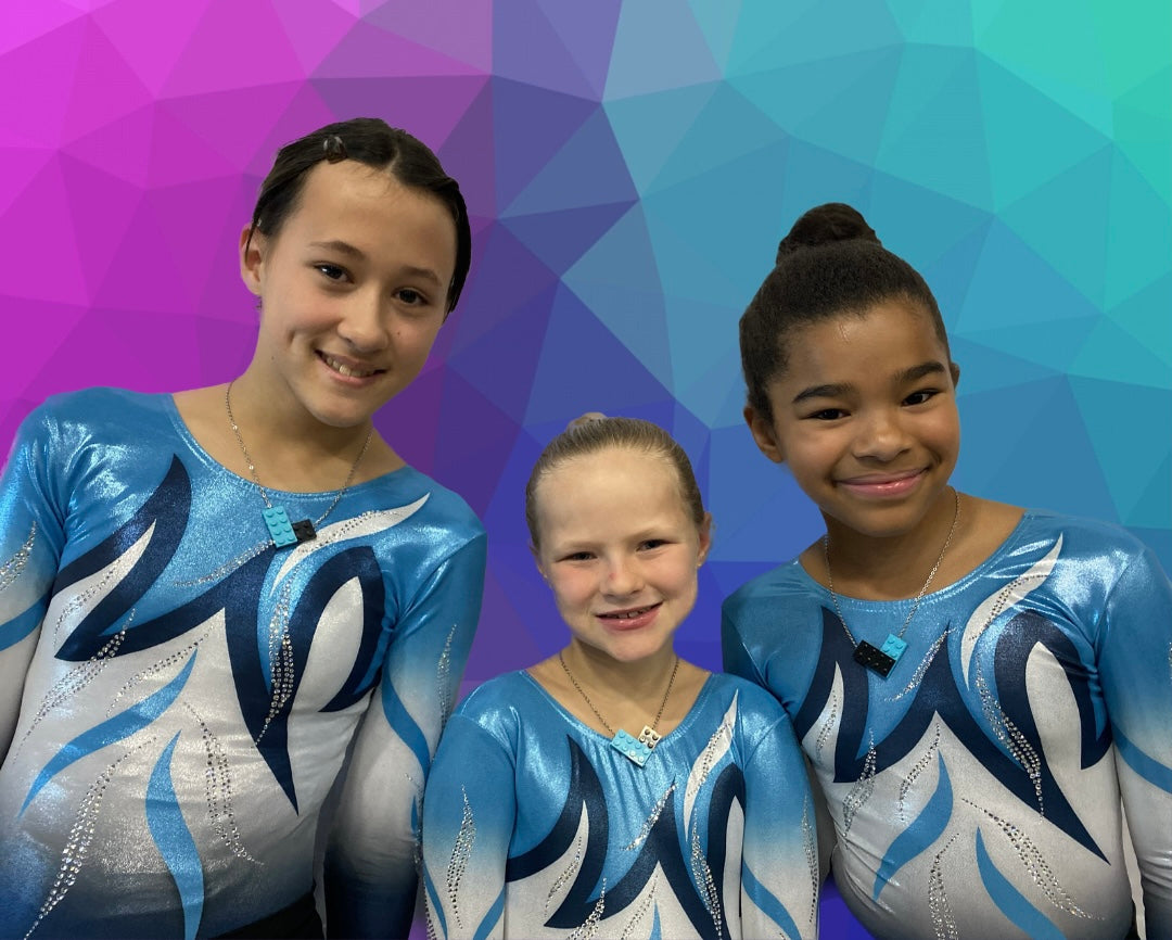 three gymnasts standing together in their team uniform wearing matching Tu Snaps necklaces made from Lego pieces