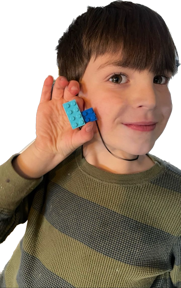 A young boy smiling and holding up his light blue  and blue Tu Snaps necklace made from LEGO pieces