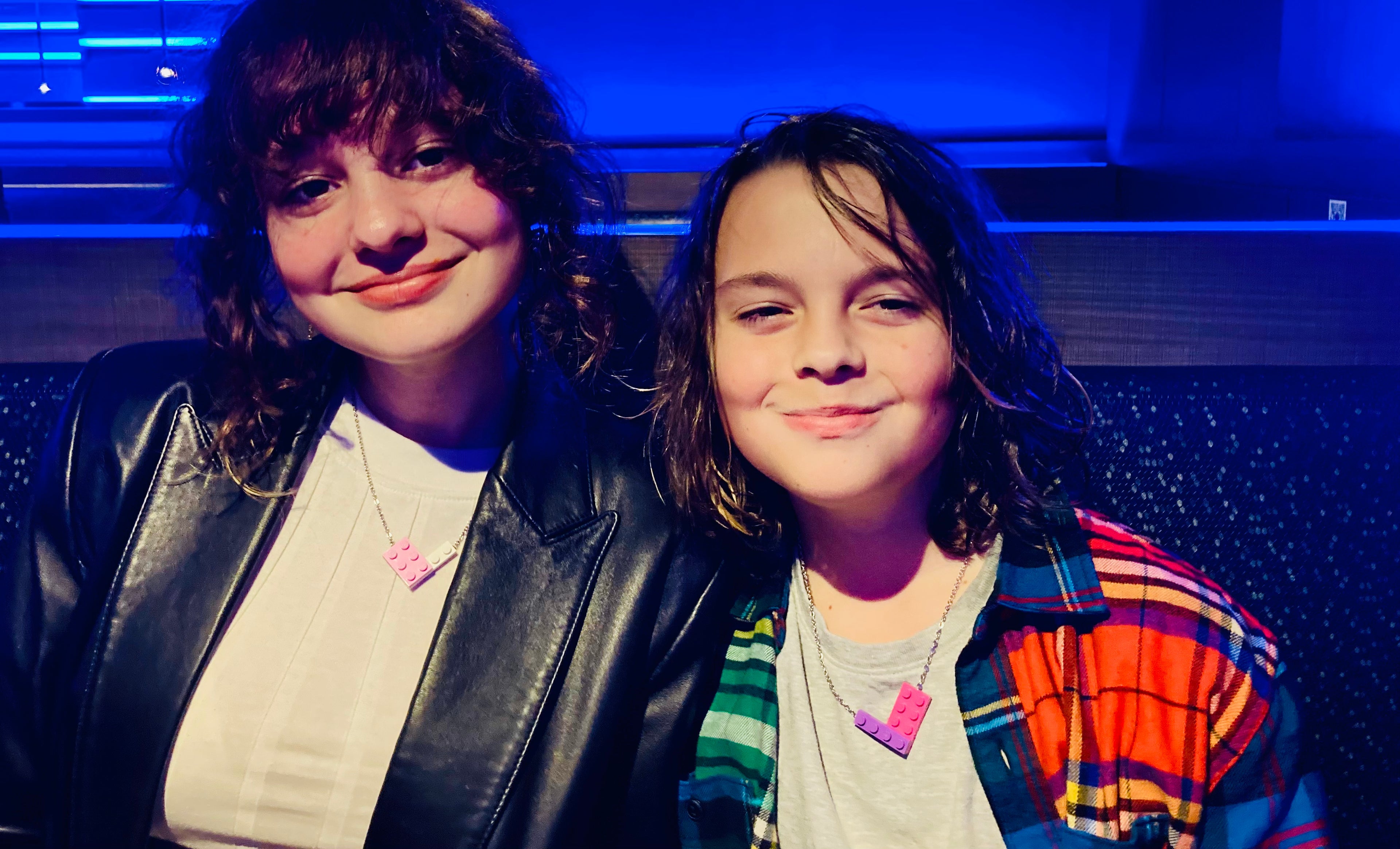 Two youth children smiling and wearing pink, white, and purple colored Tu Snaps necklaces made from Lego pieces