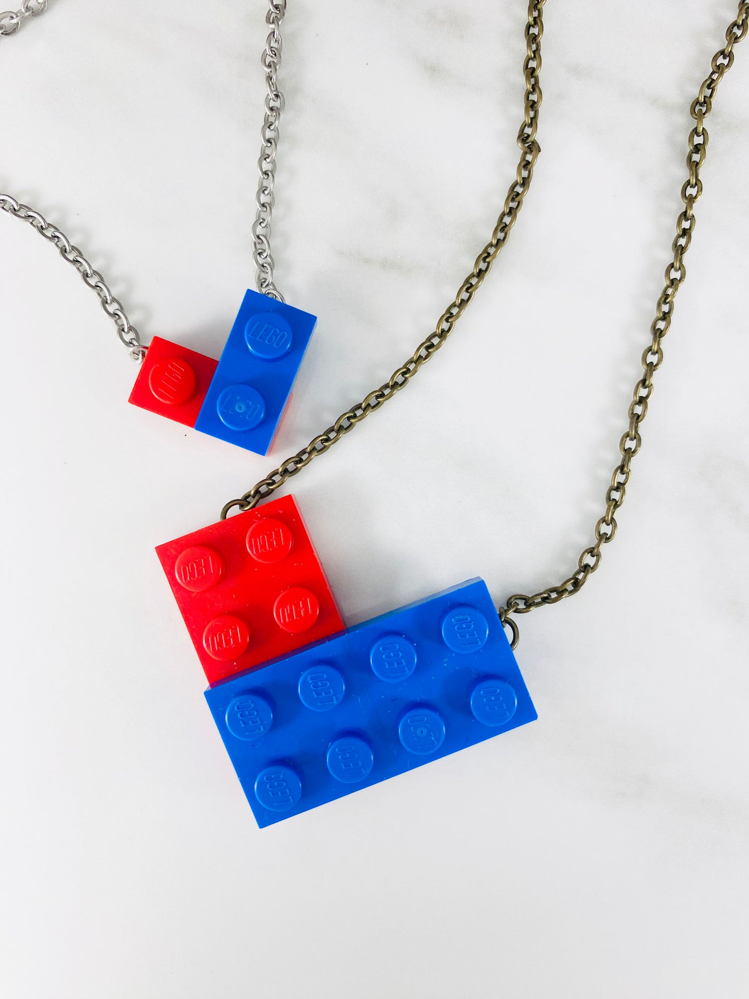 Two blue and red Tu Snaps necklaces made from Lego pieces, one in the shape of a large heart and one in the shape of a small heart